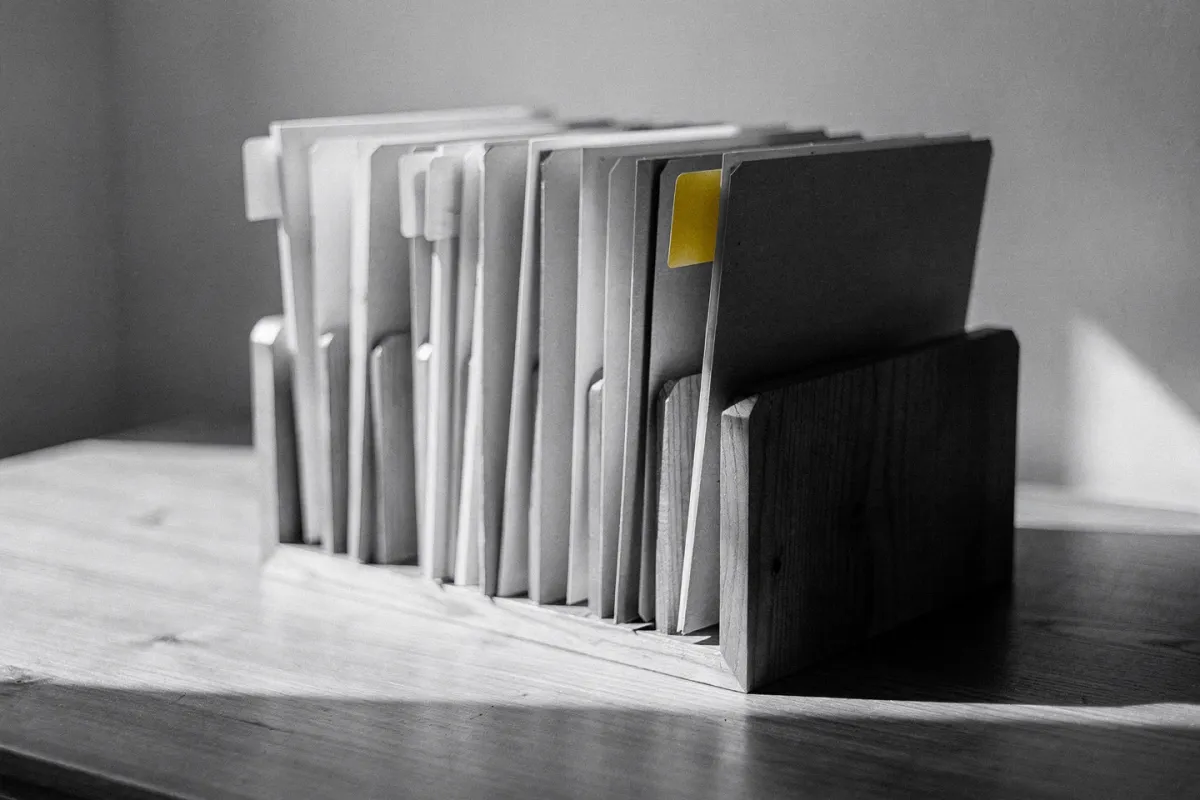 A row of file folders in a wooden desk organizer, one folder marked with a butter-yellow tab
